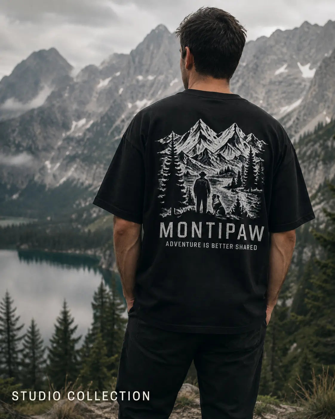 Mann trägt ein schwarzes Montipaw Oversized Shirt mit großem Bergmotiv auf dem Rücken vor einer alpinen See- und Berglandschaft.